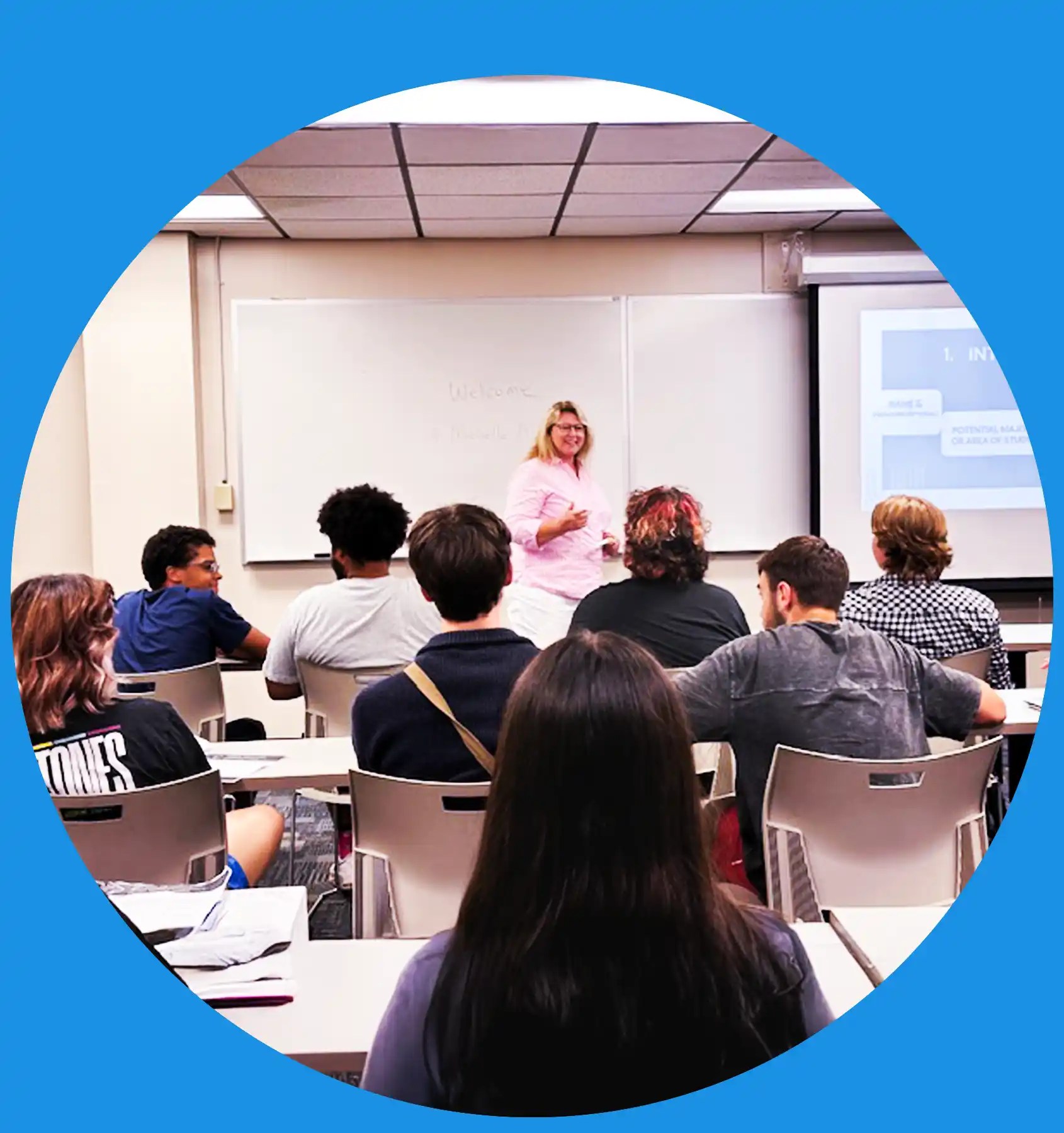 A photo of Michelle McMuffin teaching at the head of the class, she is smiling and talking, gesturing with her hands, and you can see the class is engaged.